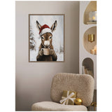 Framed canvas of a donkey wearing a red Santa hat, holding a white mug with snowy trees in the background, hanging on a beige wall above a textured chair.