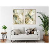 Two abstract floral canvas prints in muted green, beige, and white tones framed in light wood, hung side by side above a white sofa with patterned pillows.