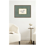 Framed wall art with 'Love You More' handwritten text in black on white, surrounded by a gold border and green vertical stripes, hanging above two cream armchairs and a brass side table.
