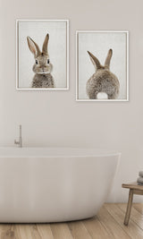 Two framed canvases above a bathtub; one shows a gray bunny's face and ears, the other shows the bunny's back with upright ears and white tail on a neutral background.
