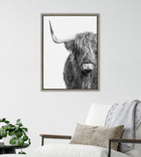 Close-up black and white portrait of a Highland cow facing forward with long shaggy hair partly covering its eyes and one visible horn, in a simple wooden frame.