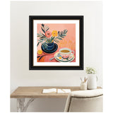 Framed painting of a blue vase with pink and yellow flowers alongside a patterned teacup on a saucer, set against a warm pink background, hanging above a rustic wooden desk.