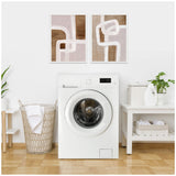 Laundry room with white front-loading washing machine centered between wicker hamper with towel and white table holding detergent and folded towels
