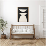 Minimalist living room with wooden slat bench, white cushions, jute rug, potted plant, and abstract black and white geometric framed canvas on white wall.