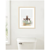Framed print above toilet of three brown bear cubs in a pale green clawfoot bathtub with white tiled walls and a woven basket on a beige rug.