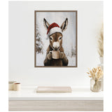 Framed canvas painting of a brown donkey wearing a red Santa hat and holding a beige mug, with snowy trees in the background, hanging on a white wall above a desk.