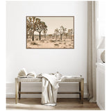 Framed canvas print of a desert landscape with multiple Joshua trees under a pale sky, hung above a wooden bench with a draped white blanket and open book.