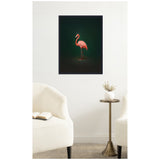 Framed canvas print of a pink flamingo standing sideways against a rich dark green background, hanging on a white wall above a small brass side table and white chairs.