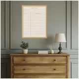 Framed fabric pinboard designed like a library card with blue lines and a beige linen texture, hung above a wooden dresser with decor and a table lamp.