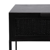 Close-up of a corner of a black wooden side table with a woven cane panel and slim metal legs