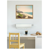 Framed vintage coastal beach photo with sandy shore, greenery, and ocean waves above a white desk featuring a wooden chair, drawing supplies, and a wooden toy truck.