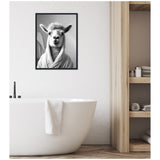 Black and white framed canvas of a llama wearing a towel robe hanging above a white freestanding bathtub with a towel draped over its edge, next to wooden shelves with rolled towels.