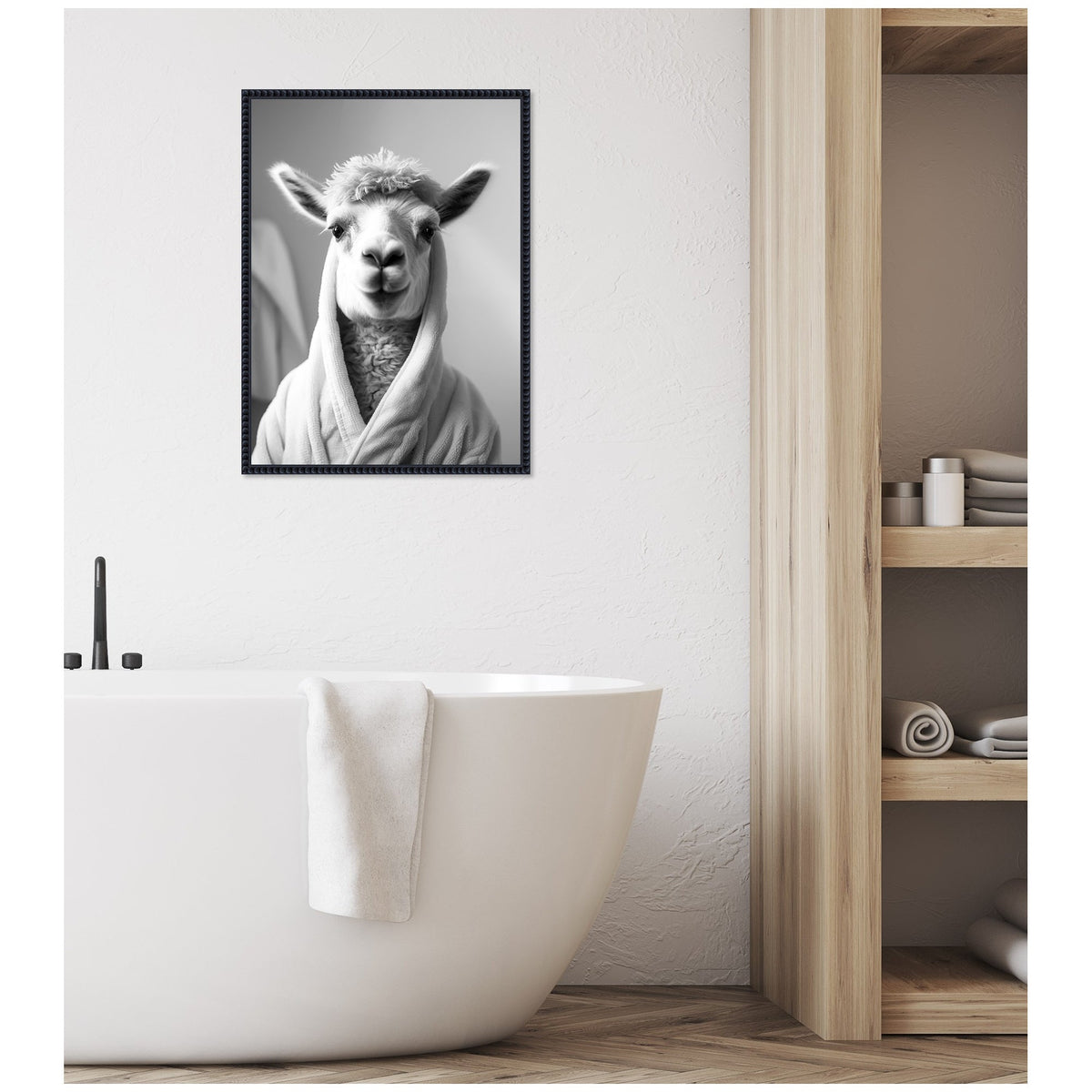 Black and white framed canvas of a llama wearing a towel robe hanging above a white freestanding bathtub with a towel draped over its edge, next to wooden shelves with rolled towels.