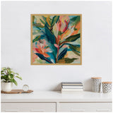 Abstract botanical canvas with bold blue, pink, green, and orange tropical leaves framed in natural wood, hanging above a white surface with plants and books.
