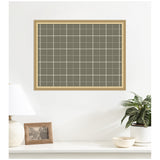Framed sage green fabric pinboard with white grid lines hanging on a white wall above a white surface with a lamp, photo frame, plant, and bowl.