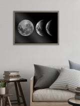 Framed black and white print of three moon phases from full to crescent mounted on a white wall above a beige sofa with gray and striped pillows.