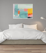 Abstract painting with teal, coral, yellow, and gray color blocks in a white frame hanging above a white bed against a gray wall, with a white desk lamp on the right.