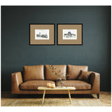 Two black-framed vintage postcard prints of London and Paris landmarks with brown mats, hanging above a brown leather sofa with a pillow and a light wood coffee table.