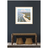 Framed coastal landscape painting with blue water, sandy shore, and green marshland against a cloudy sky, hung on a dark blue wall above a rustic wooden bench with woven baskets below.