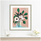 Framed floral painting with white flowers and green leaves against a soft blush pink background, hung above a minimalist white shelf with glass decor.