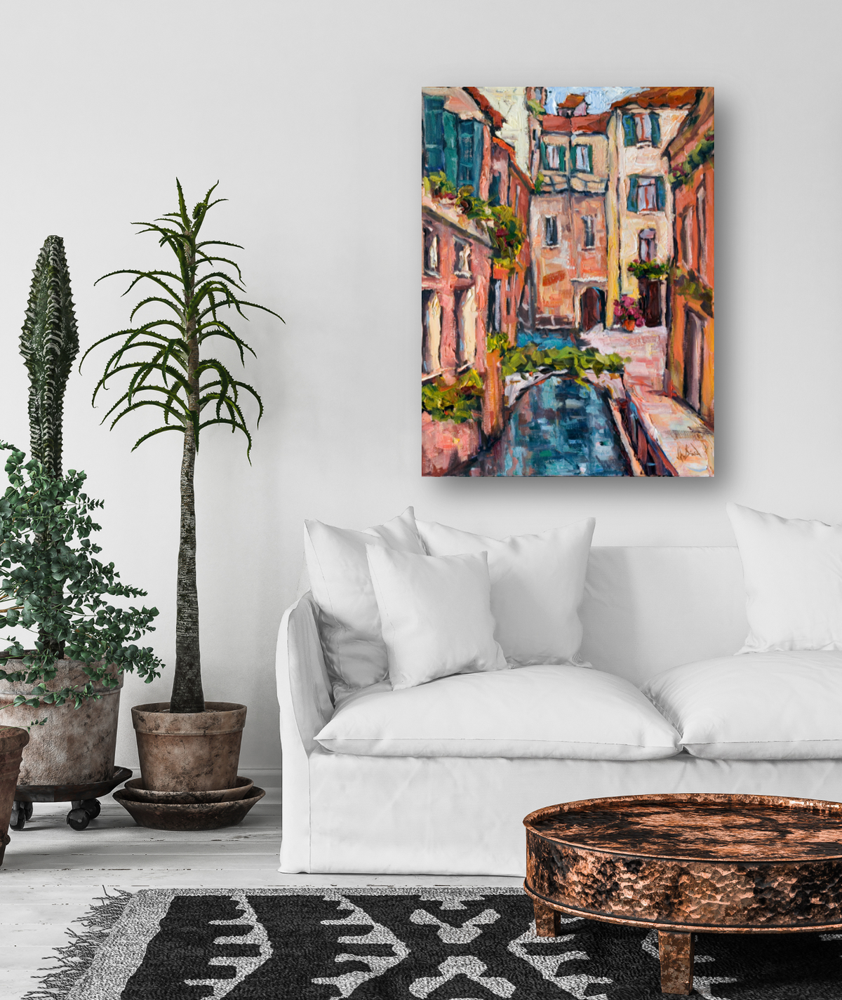 Vibrant painting of a narrow canal with colorful buildings in shades of pink, orange, and blue, hanging above a white sofa in a minimalist living room.