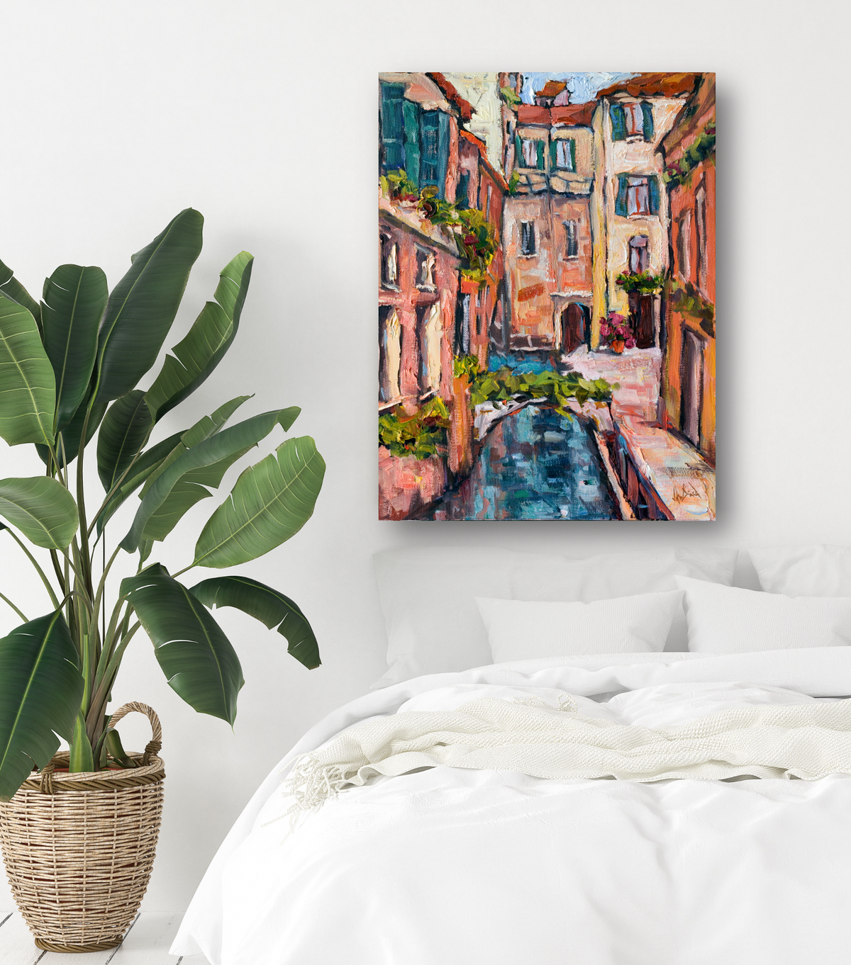 Colorful impressionist painting of a narrow canal with stone buildings and a small arched bridge, displayed above a white bed next to a large potted plant.