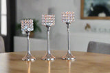 Set of three silver aluminum candle holders in small, medium, and large sizes, each topped with a cube of clear, faceted crystals, arranged on a wooden table.