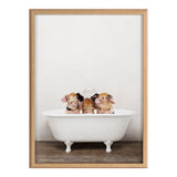Three piglets with pink and brown spots sitting inside a white vintage clawfoot bathtub on a wooden floor against a plain white wall, framed in light wood.