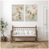 Two-paneled canvas wall art with soft pink, green, and beige floral abstract patterns above a wooden daybed with white cushions in a bright, minimalist room.