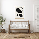 Minimalist living room with light wood bench topped by white cushions, natural woven rug, potted plant in basket, and framed black abstract geometric art on white wall