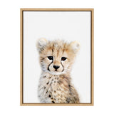 Framed canvas artwork of a young cheetah cub with soft fur and expressive dark eyes on a white background, surrounded by a light wood frame.
