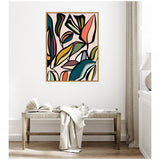 Abstract botanical wall art with overlapping stylized leaves in muted shades of blue, coral, mustard, and green, framed above a wooden bench with a draped cloth and open book.