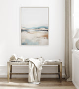 Abstract landscape painting with soft blue and beige tones above a wooden bench holding an open book and a draped light fabric in a bright minimalist room.