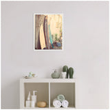 Framed canvas featuring two vintage surfboards, one beige and one teal, leaning against a weathered wooden wall with plants nearby, hanging above a white shelf with toiletries and towels.
