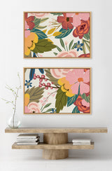 Two framed canvas prints featuring colorful floral patterns with pink, red, yellow flowers, and green leaves, arranged vertically above a wooden console table.