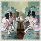 Two black-and-white dogs wearing pink robes sitting on floral-patterned armchairs facing forward, with a small wooden table between them holding two white coffee cups and a vase with daisies.