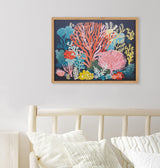 Framed coral reef illustration with vibrant red, pink, yellow, and blue coral shapes on a dark blue background, hanging above a light wood bed frame with white pillows.