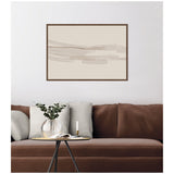 Framed abstract wall art with flowing neutral beige and taupe brush strokes above brown couch with beige cushions and round glass vase on small table.