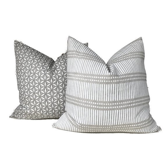 Two decorative throw pillows: one with a geometric floral pattern in muted gray tones, and the other with horizontal stripes and dots in chalk and soft gray.
