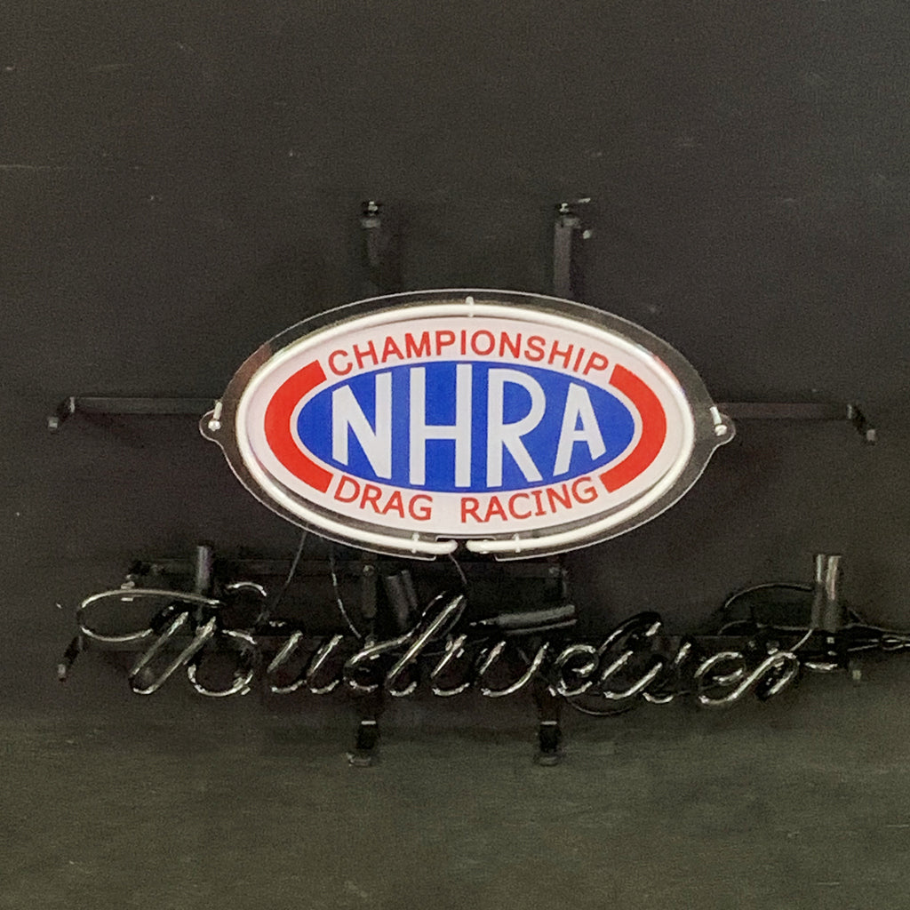 Oval neon sign with blue center reading 'NHRA' and red text 'Championship Drag Racing' around it, above cursive 'Budweiser' neon lettering on black background.