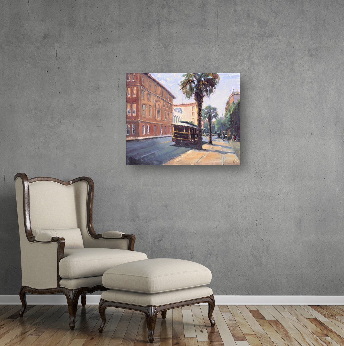 Canvas print of a street scene with a vintage trolley, palm trees, and sunlit sidewalks, displayed on a gray wall above a cream armchair with wooden legs and matching ottoman.