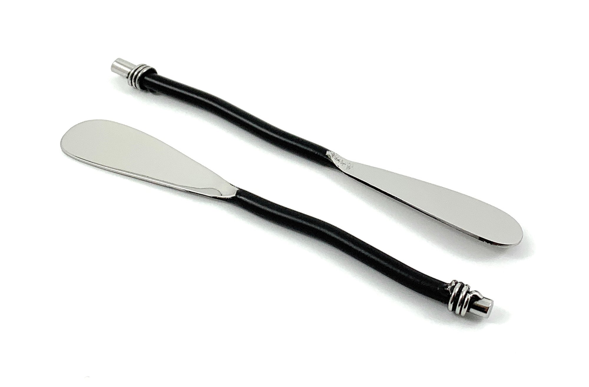 Set of six Vibhsa black silverware butter spreaders resting on a wooden surface alongside cheese and crackers