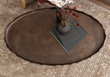 Oval coffee table with a scalloped-edge dark brown surface, decorated with a black matte vase holding red dried flowers and two black books underneath, on a patterned rug.