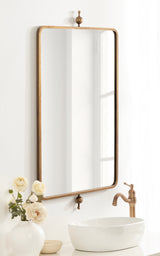 Tall rectangular wall mirror with rounded corners and a slim wood frame, mounted above a white oval vessel sink and a bronze faucet, decorated with white roses in a vase.
