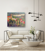 Impressionist canvas painting of a hillside town with a clock tower surrounded by colorful rooftops and lush greenery, displayed above a modern white sofa in a minimalist living room.