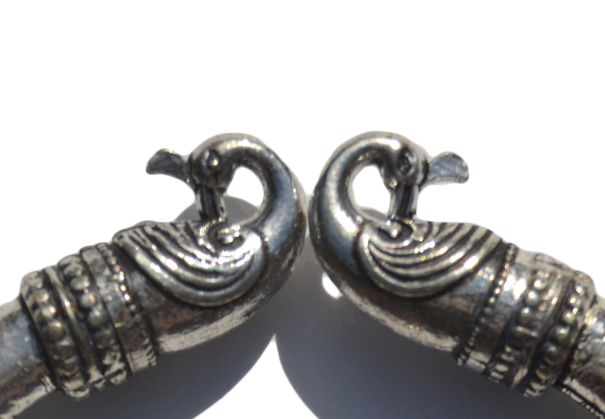 Antique silver-toned Viking bracelet ends shaped as Norse peacock heads with detailed curved necks and dotted patterns on a white background.