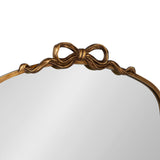 Top section of an arched mirror framed in metallic gold with a sculpted ribbon-shaped decorative bow centered at the peak of the frame.