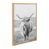 Black and white portrait of a Highland cow with long curved horns standing in a grassy field with hills in the background, framed in a light wood frame.