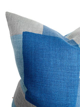 Close-up of a pillow corner featuring a color-blocked pattern with indigo blue, light blue, and gray woven fabric sections.