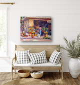 Artist-enhanced canvas print depicting a fruit and vegetable stand with colorful produce and a person in a pink shirt, hanging above a wooden bench with black-and-white checkered pillows.